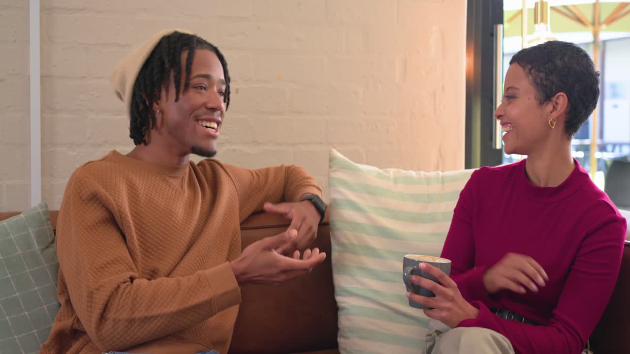 Diverse friends sharing story with hand gesture sipping coffee from mugs on leather sofa
