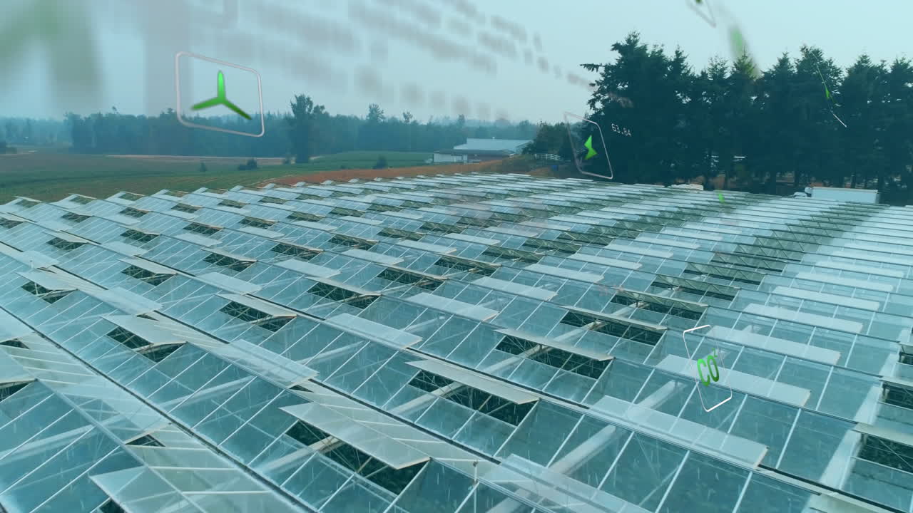 Wind turbines rotating above glass-roofed greenhouses in rural landscape setting