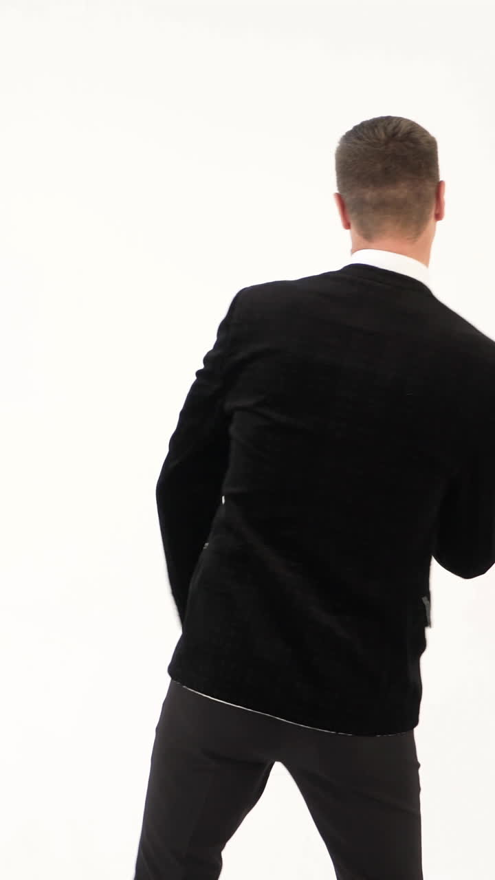fun man in a black suit with a bow tie is showing dance of dancer on the white background Vertical video