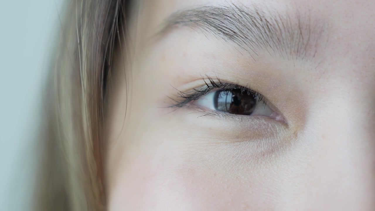 柔らかな自然光の中で、ナチュラルメイクのアジア人女性の目のクローズアップ。詳細な虹彩、まつげ、表情を捉えている。