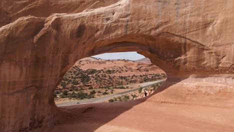 drone volando en el agujero del arco de wilson revelando la autopista 191 de los estados unidos en la distancia en un día soleado en moab, utah, estados unidos