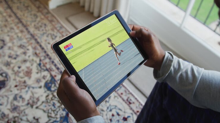 Composite of man sitting at home, watching athletics running event on tablet
