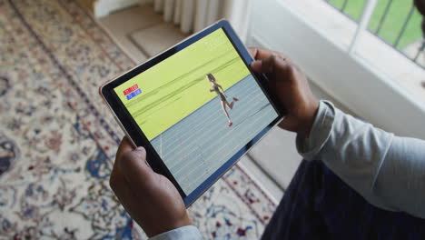 compuesto de un hombre sentado en casa, viendo atletismo corriendo evento en la tableta
