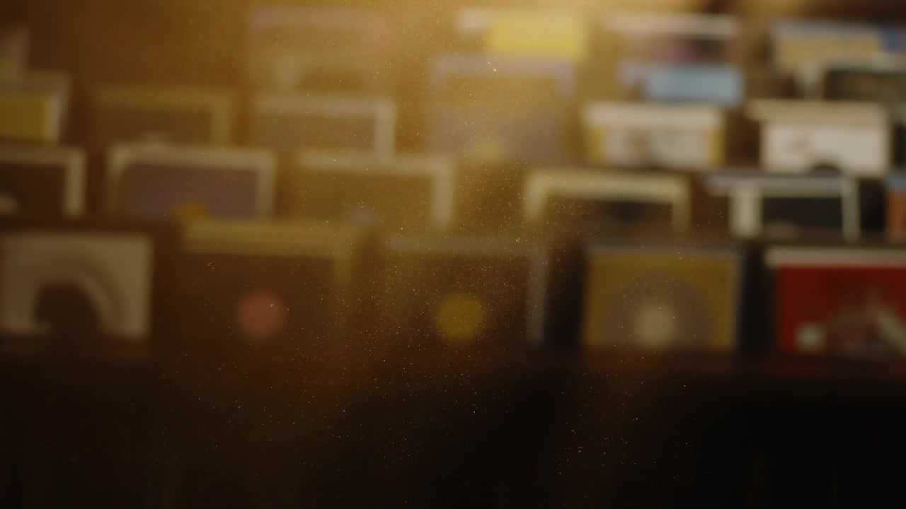 Particelle di polvere sospese catturano una calda luce dall'alto mentre un morbido bokeh e un delicato bagliore velano file sfocate di oggetti rettangolari su scaffali interni, creando una profondità atmosferica accogliente e un movimento sottile