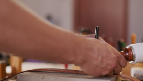 master makes hole in belt with punch and hammer at table