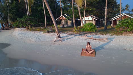 Increíble-Vuelo-De-Vista-Aérea-Levanta-El-Dron-De-Ojo-De-Pájaro-De-Una-Chica-De-Yoga-Sentada-Bajo-Una-Palmera-En-La-Isla-De-Koh-Kood-De-La-Playa-De-Seacret-Al-Atardecer-Tailandia,-Día-2022