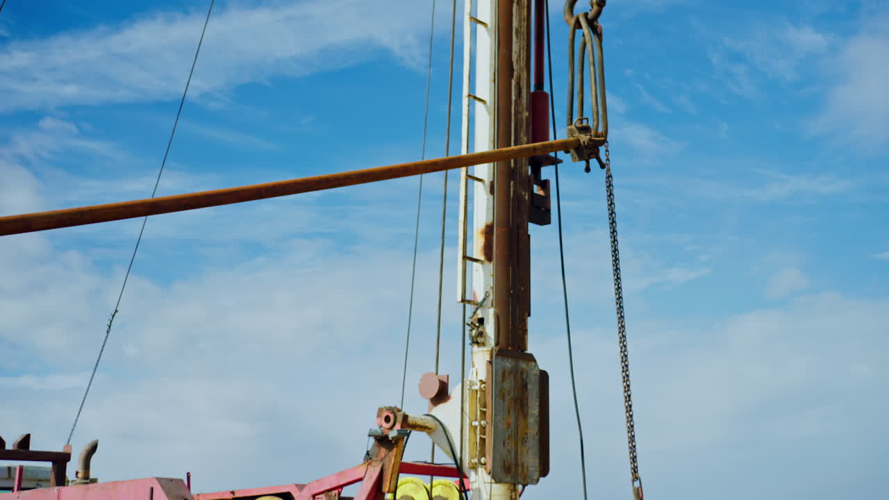 Men wearing protective helmet work near the truck with drilling equipment. A hook rises the metal pipe up.
