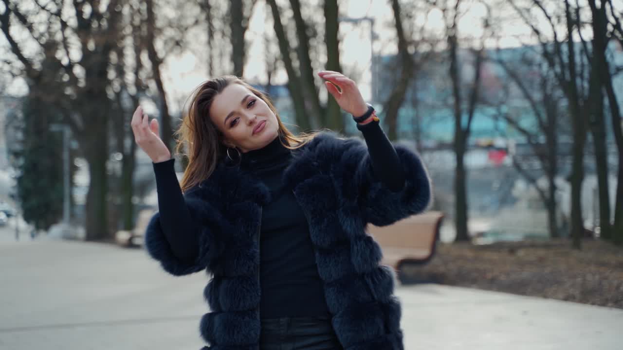Portrait of a sexy girl outdoors. Attractive woman in a luxury fur coat in the park. Beautiful young model on the city street background. Slow motion.