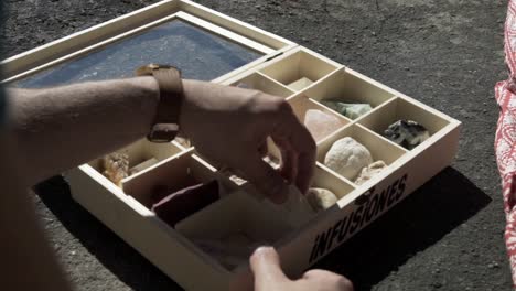 a square-shaped box contains numerous types of rocks with specific attributes, and the man is looking at each one