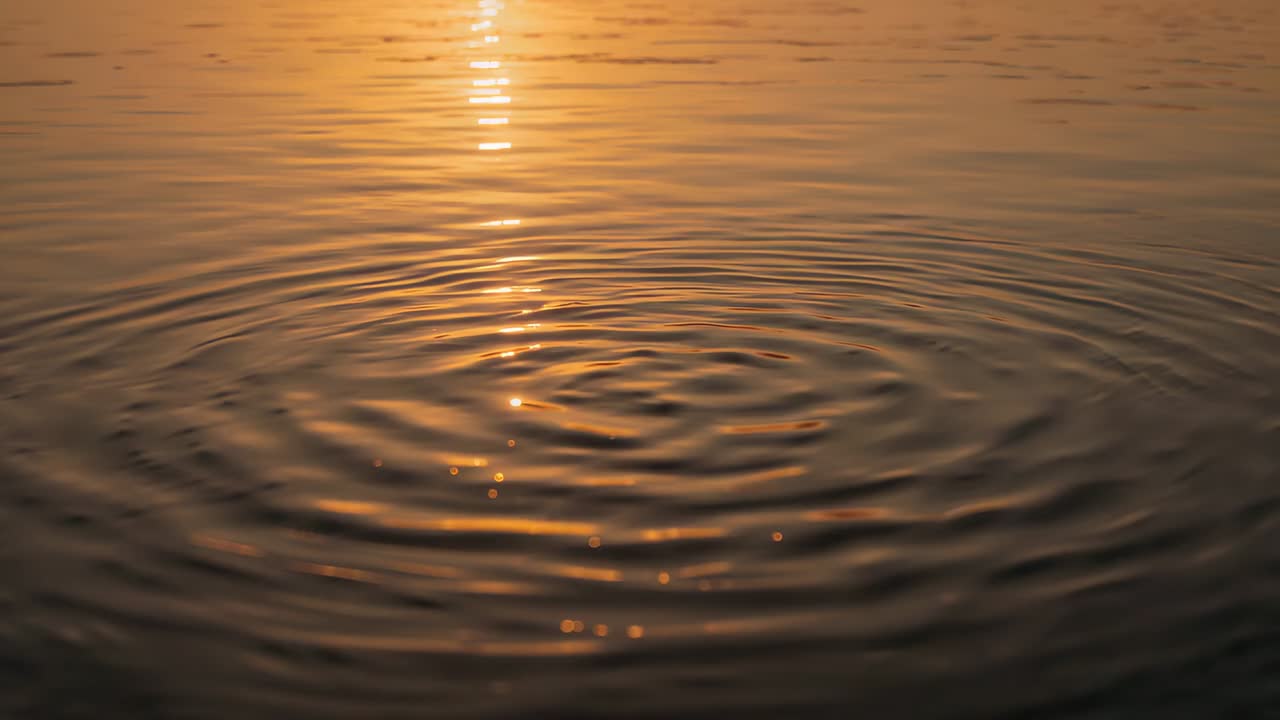 Onde concentriche che si espandono dopo un impatto centrale sull'acqua calma al tramonto, riflettendo una fascia dorata
