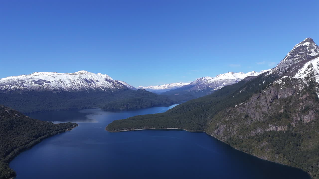 High altitude drone shot over Lago Futalaufquen, Parque Nacional los Alerces. Snowed peaks with glaciers contrast with deep blue water and sky. Shot 4K-60fps.