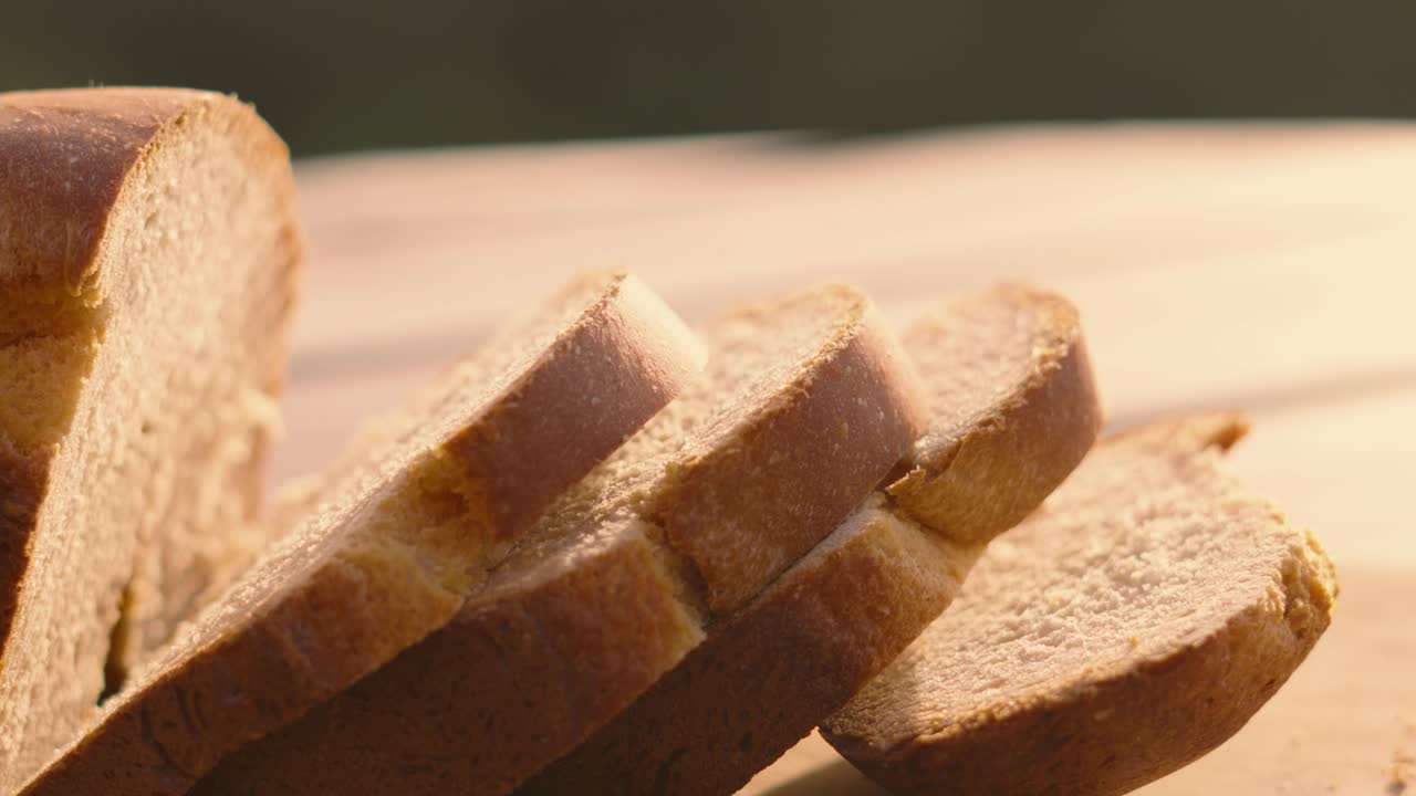 Slices of Freshly Baked Homemade White Bread on Wooden Chopping Board Outside in Natural Morning Sunlight with Shallow DOF. Home Baking Footage with Simple Healthy Ingredients 4K.