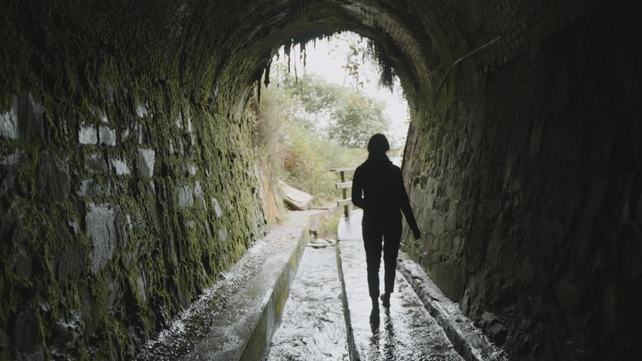 Person walking through a moss-covered stone tunnel