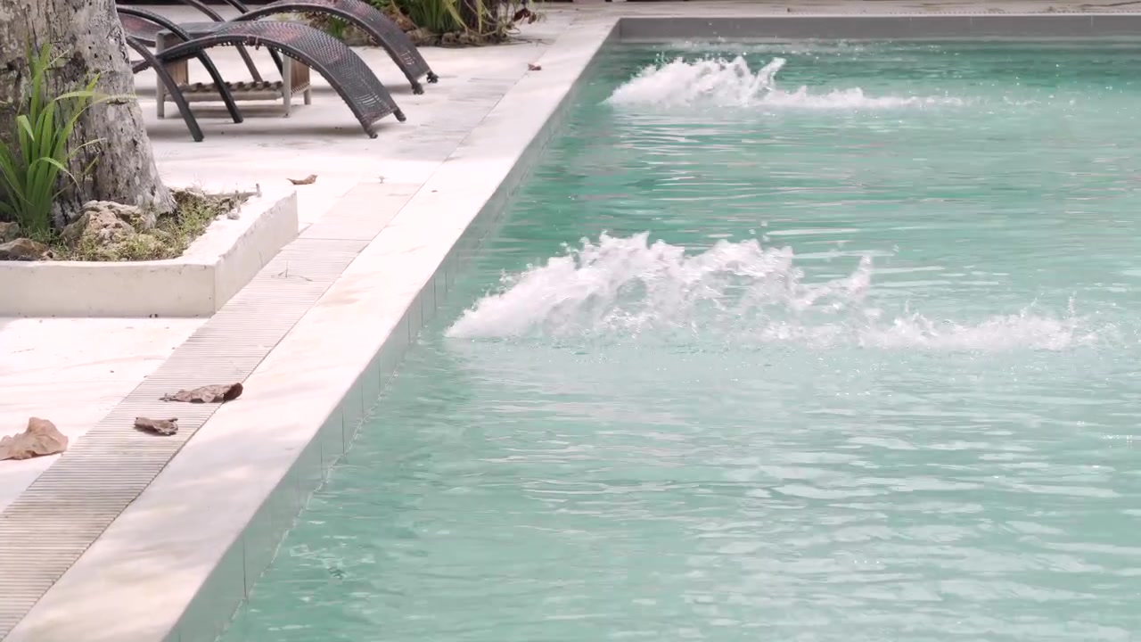 Elegant outdoor swimming pool with crystal-clear water, bubbling water jets, and contemporary lounge chairs in soft daylight.