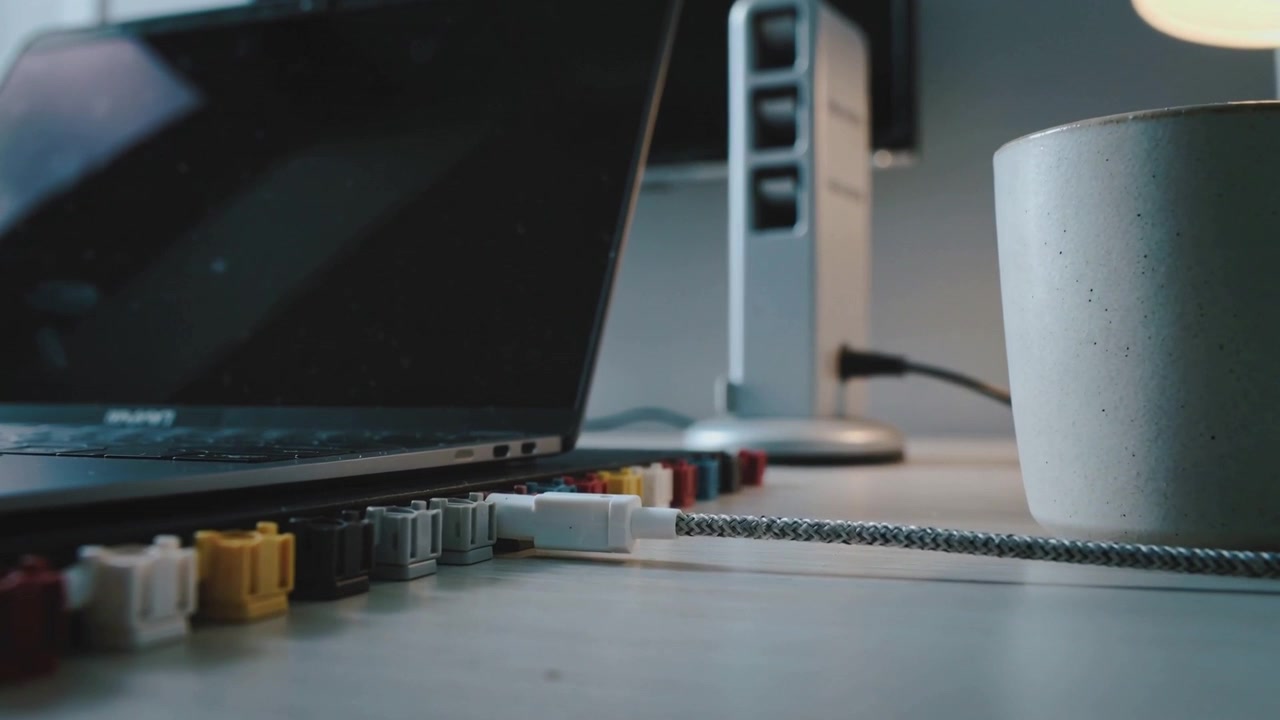 Camera panning desk revealing braided cable, white plug near laptop and color clips showing texture