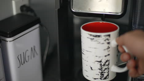 grabbing a birch themed red and white mug from a home coffee maker