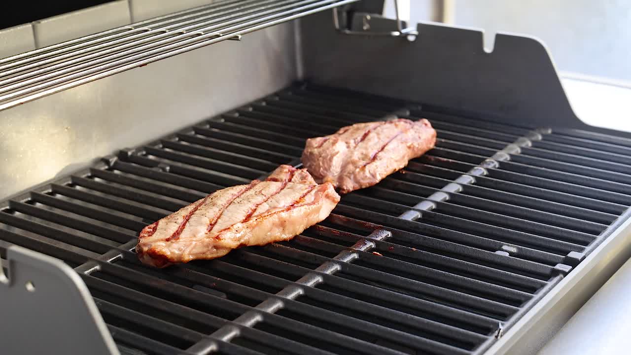 Beef steak grilling on a barbecue with tongs in a sunlit outdoor setting. Captures the cooking process and grill marks