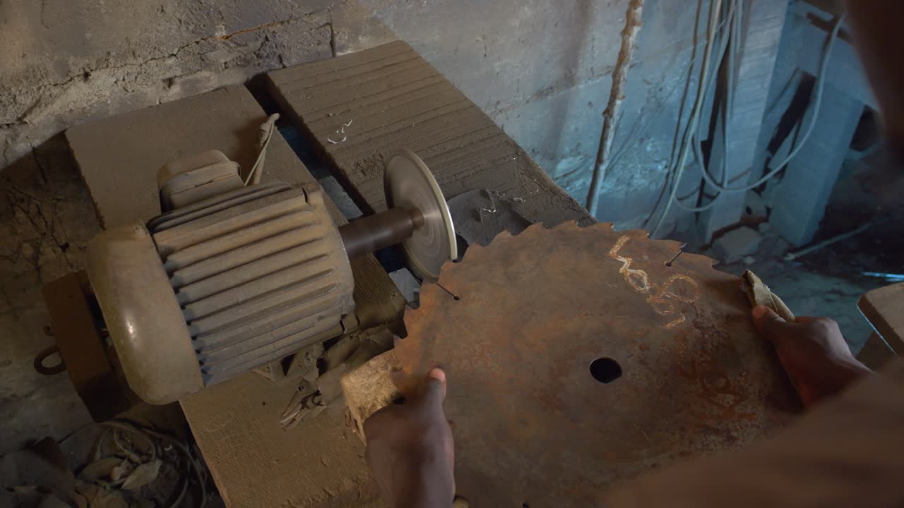 African worker Sharpens a metal saw with automatic polisher closeup shot in humble work shop, Ghana