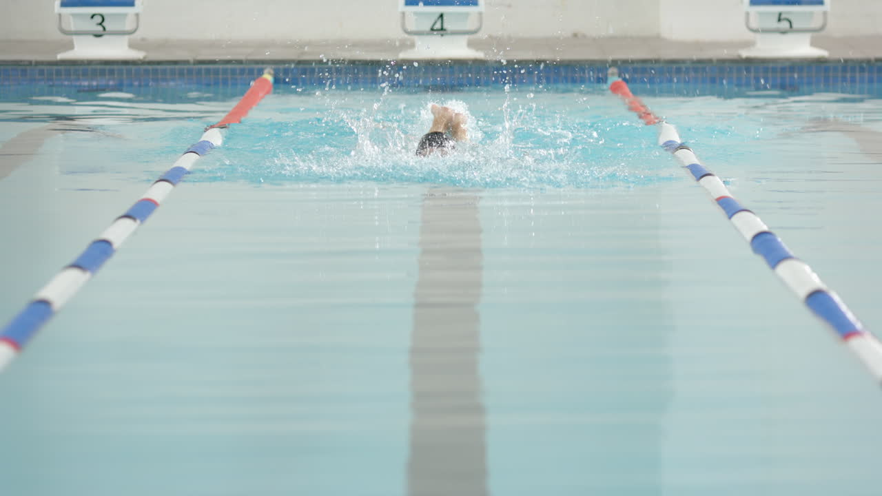 Swimmer performing butterfly stroke in swimming pool, focusing on technique, copy space