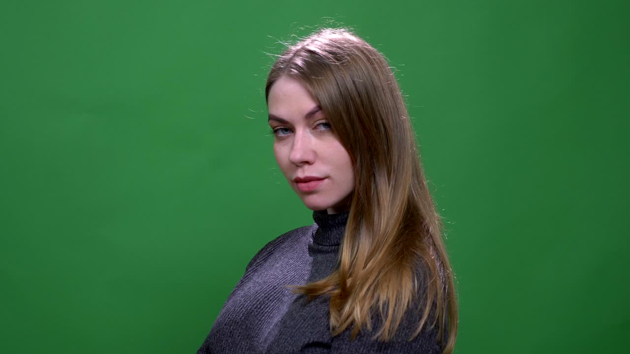 매력적인 금발 모델이 녹색 크로마키 배경에 심각하게 고립되어 유행적으로 포즈를 취하고 있습니다.