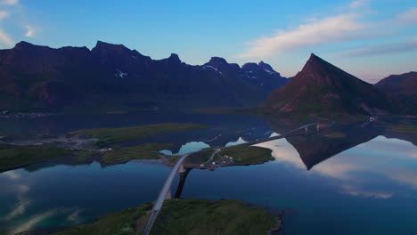 Aerial-circling-shot-of-Fredvang-Brigde-during-midnight-sun-with-scenic-view-of-mountain-in-Background