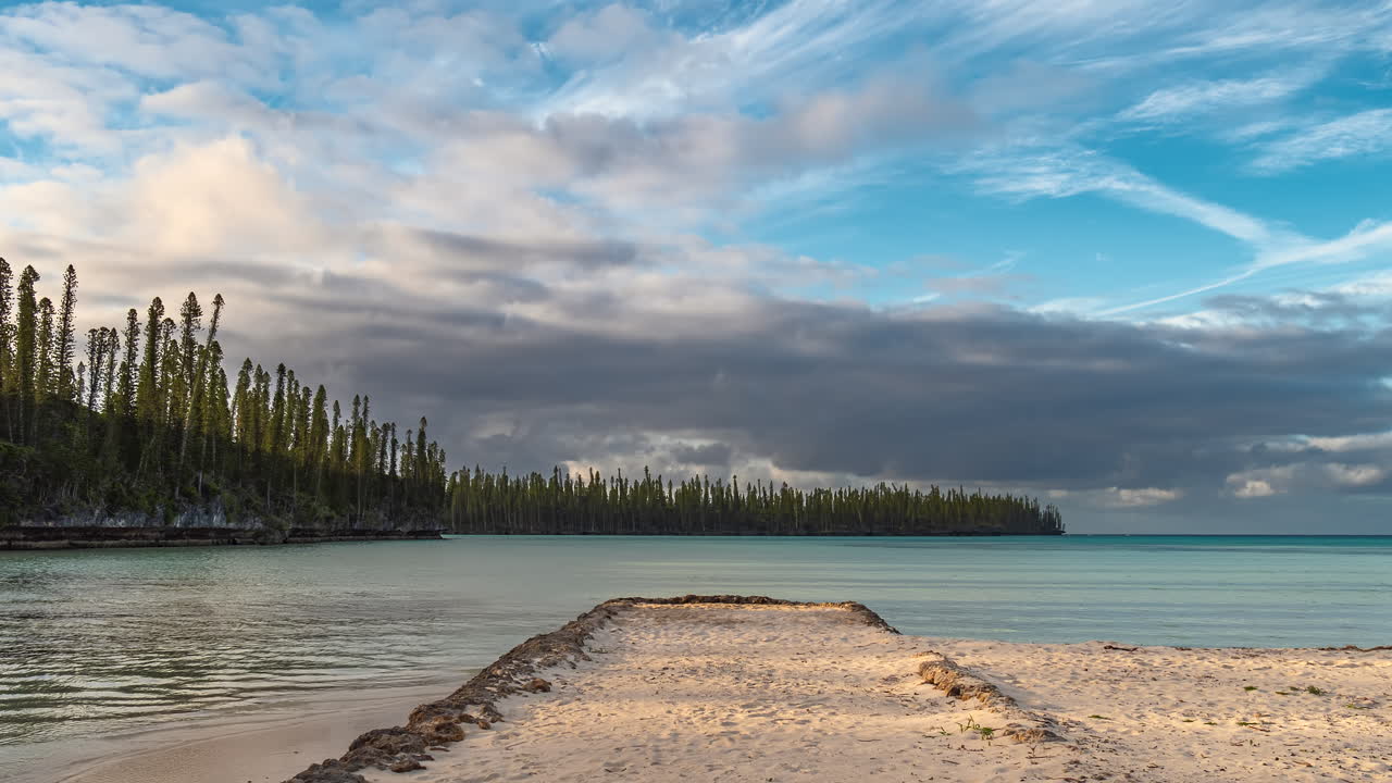모래로 뒤덮인 빈티지 보트 선착장은 뉴칼레도니아의 파인 섬 멀리 해안에 있는 원주형 소나무가 있는 그림 같은만으로 향합니다 - 저속 클라우드스케이프