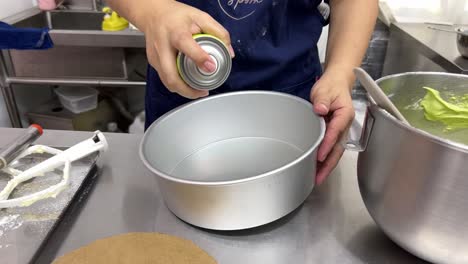 Spraying-oil-and-greasing-the-cake-mould-before-pouring-the-mixtures,-professional-pastry-chef-in-action,-close-up-shot