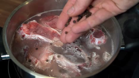 añadiendo pimienta entera a la olla con huesos de carne para el caldo, cerrar la cámara lenta