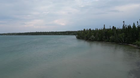 Eine-Bewegte-Luftdrohnenaufnahme-Des-Clearwater-Lake-Vom-Sunset-Beach-Am-Rande-Des-Pas-Gebiets-Im-Sommer-2023-An-Einem-Bewölkten-Tag