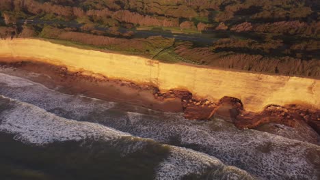 high aerial top view of the cliffs at beautiful sunset with the water waves in the ocean touching the sand too and fro in acantilados de mar del plata, argentina