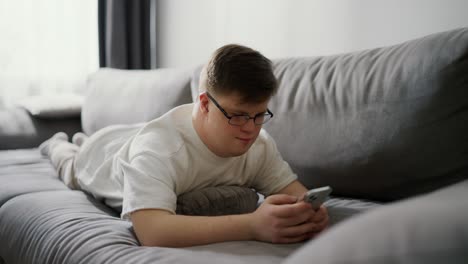 smiling man with down syndrome using cellphone while resting on couch at home