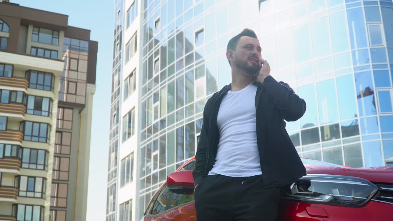 Giovane uomo d'affari in piedi vicino all'auto mentre parla allo smartphone vicino a un centro direzionale