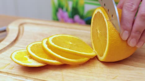 manos de mujeres amas de casa cortadas con un cuchillo naranja fresca en la tabla de corte de la mesa de la cocina