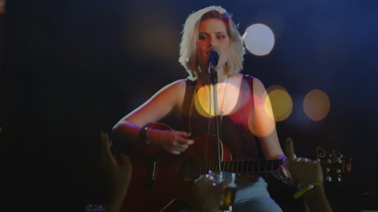 teenage girl strumming acoustic guitar and singing on music stage, with animated bokeh spotlights