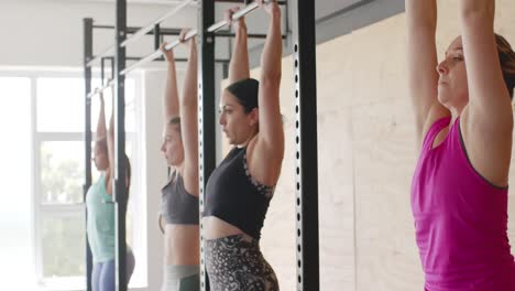 entrenamiento grupal de mujeres diversas sin alteración en el gimnasio haciendo abdominales colgantes de barras, en cámara lenta