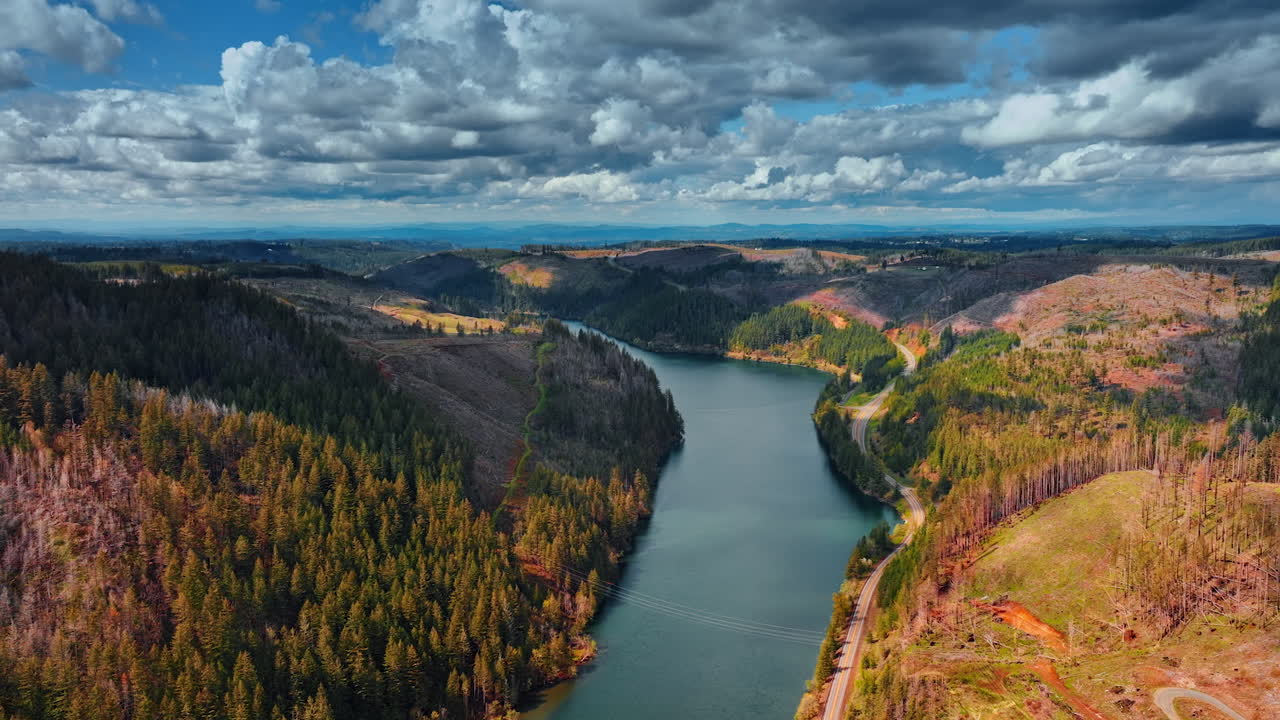 Grey river reflecting the cloudy sky crosses the mountainous area. Dramatic cloudscape is above the scenery with rocks and pine tree woods. Top view.