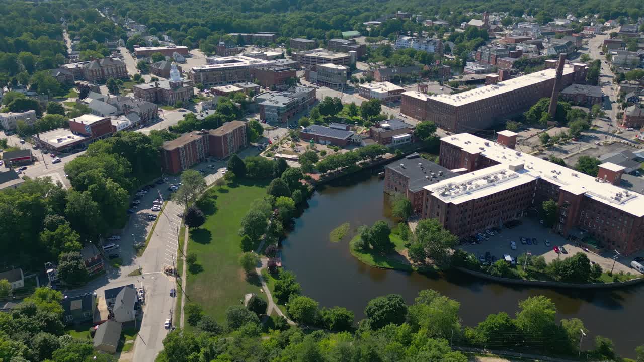 High pull-back drone shot of the mill and river in historic downtown Dover, NH, USA. It reveals the mill, children's museum and main street. There are red brick buildings and light traffic