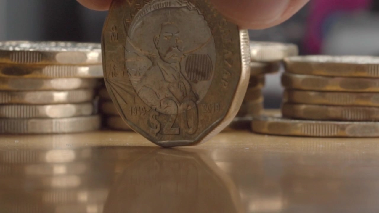 Macro close up of Mexican 20 peso coin spinning between stacks of coins on a wooden surface, highlighting currency, monetary value, and the motion of the rotating coin.