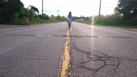 little girl walking on the yellow line dividing lanes of asphalt road with cracks