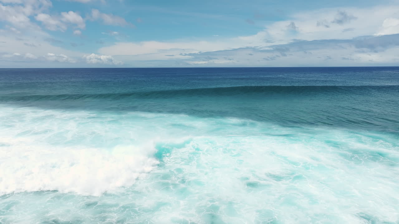 Slow motion smooth aerial pullback of foamball from crashing wave glistening on fringing coral reef