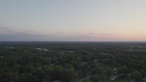 An-aerial-shot-of-asphalt-road-with-green-trees-at-sunset-in-autumn