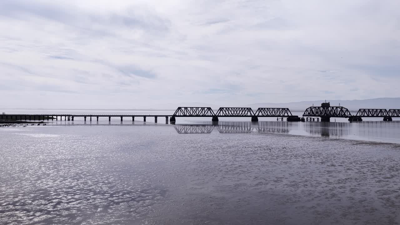 Vista aerea panoramica dello storico e abbandonato ponte ferroviario di Dumbarton, una struttura a traliccio in acciaio che attraversa le calme acque della Baia di San Francisco a Newark, California, in una giornata nuvolosa