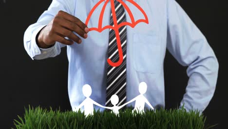 Mid-section-of-businessman-with-cutout-paper-chain-family-with-the-protection-of-umbrella