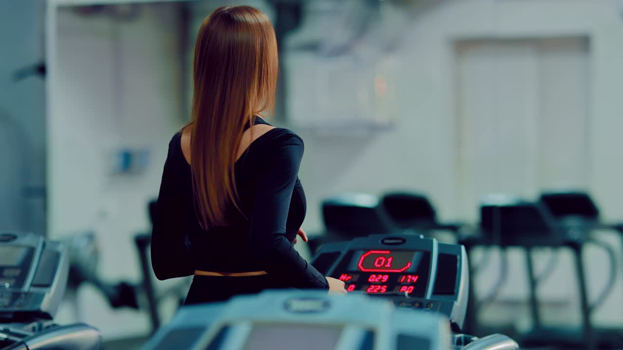 Woman with long hair runs on a treadmill in the gym. Exercise in the gym. View from the back.