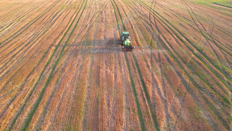 Vista-Aérea-Del-Tractor-Navegando-En-Una-Enorme-Granja-Mientras-Rocía-Pesticida