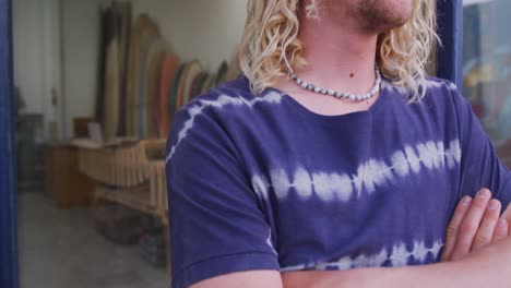 caucasian male surfboard maker leaning on a door frame of the entrance with his arms crossed