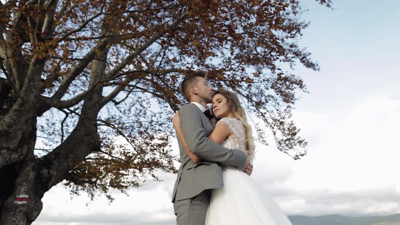 Lovely young newlyweds bride groom embracing on cloudy sky background, wedding couple family in love