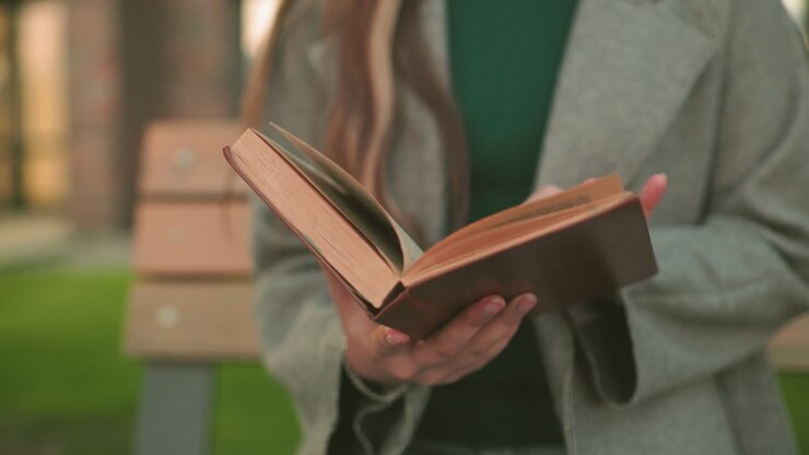 Primo piano di una donna che tiene aperto un libro all'aperto, con le dita che sfogliano le pagine con del testo visibile, per sottolineare l'apprendimento, lo studio e uno stile di vita riflessivo