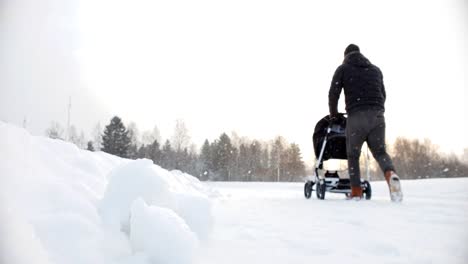 Static-slow-motion-shot-of-father-on-paternity-leave-walking-baby-stroller-in-stormy-winter-weather