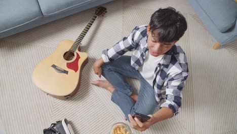 young person using phone in living room with guitar and snacks